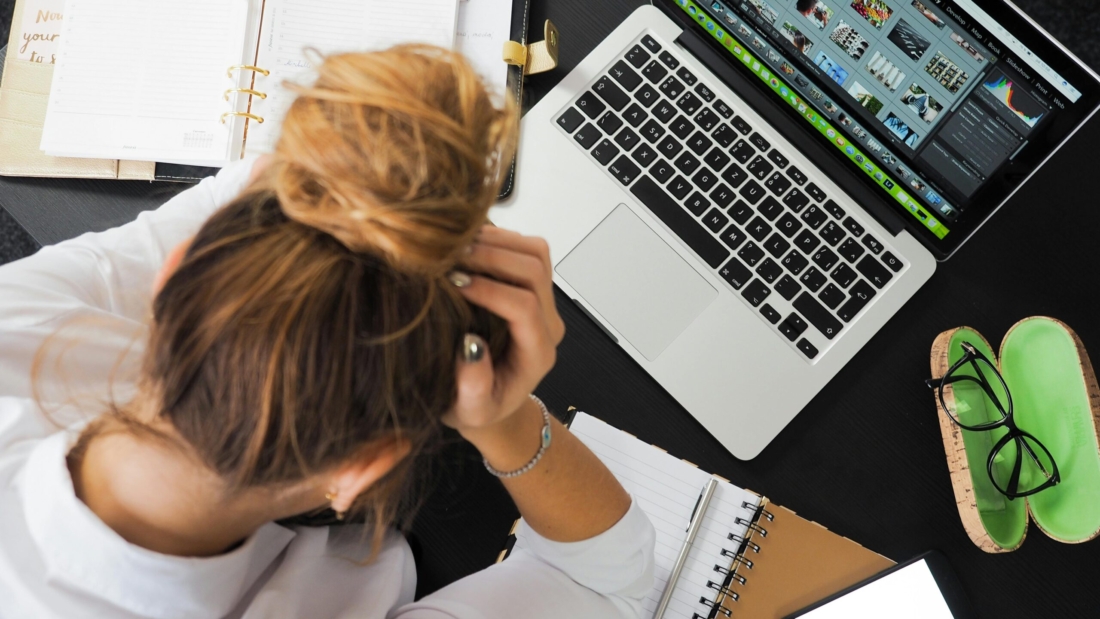 Overhead view of a stressed woman working at a desk with a laptop, phone, and notebooks.